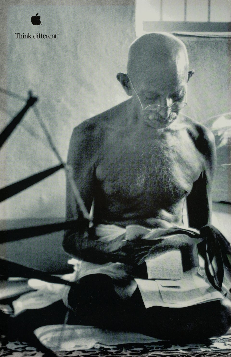 Apple’s Think Different poster: Gandhi seated beside a spinning wheel, with a small black Apple logo and the campaign line.